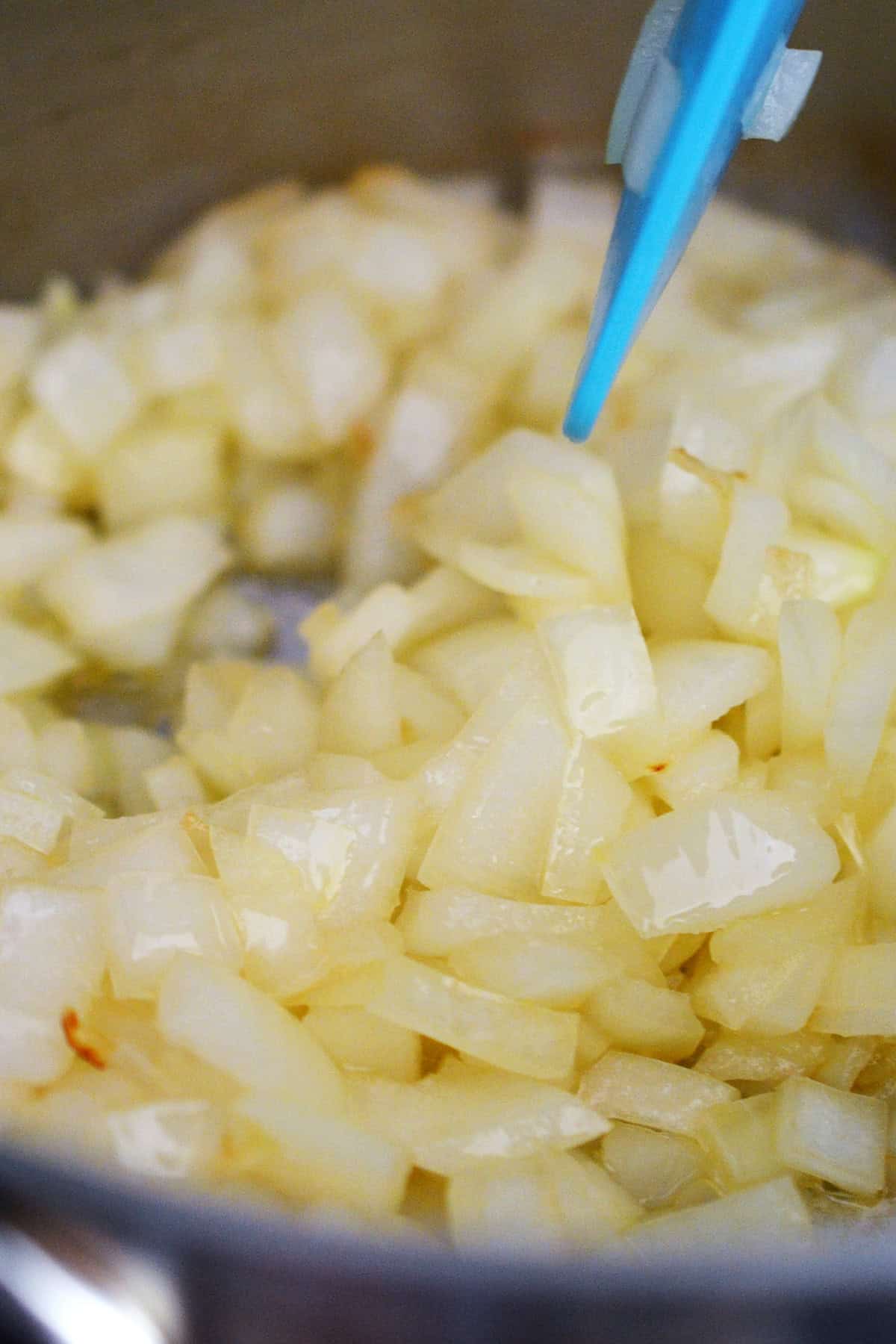 A closeup view of diced onions sautéing in a small saucepan to make a gluten free gravy.