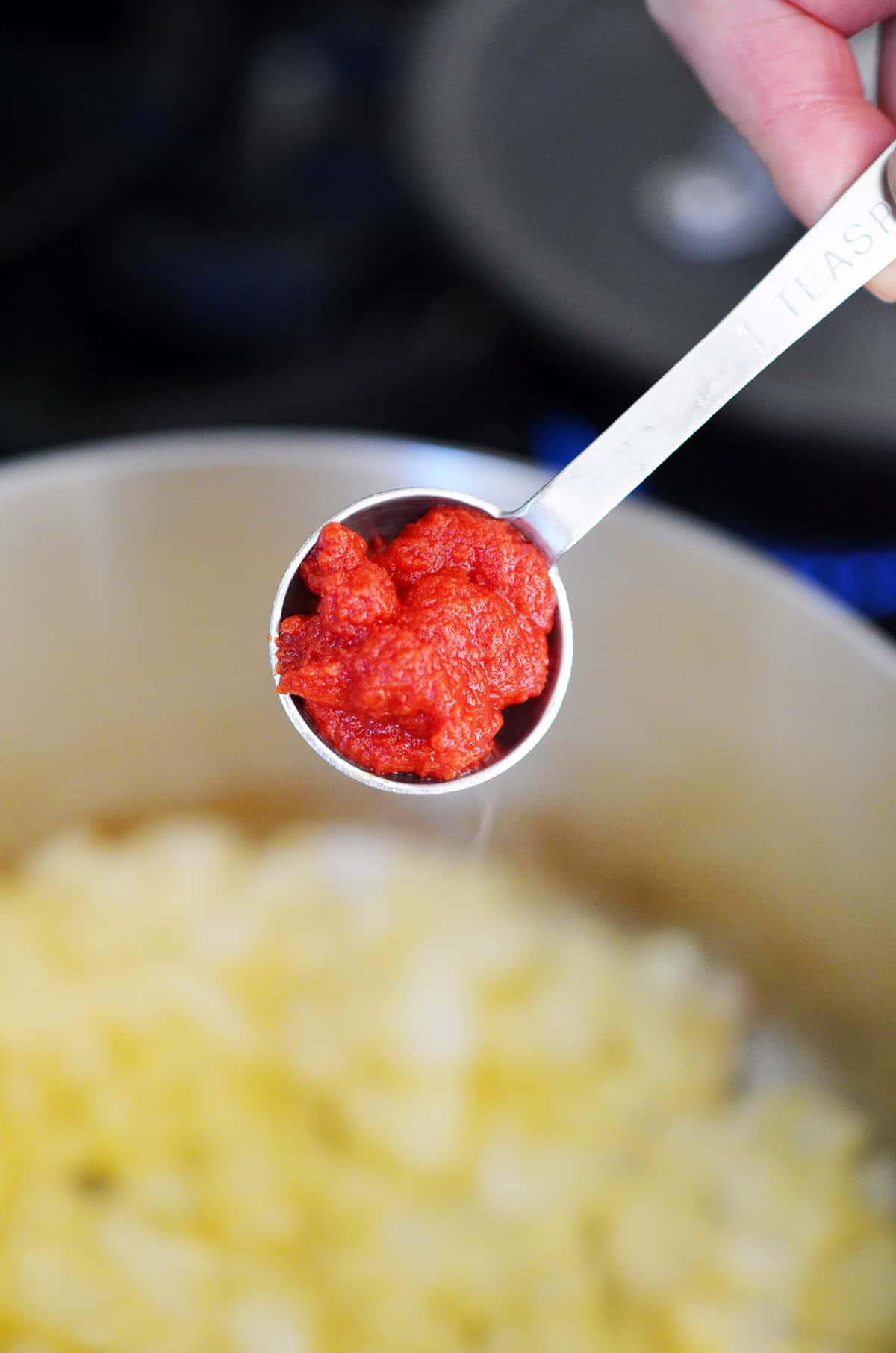 Adding a spoonful of tomato paste to a saucepan filled with sautéed diced onions.