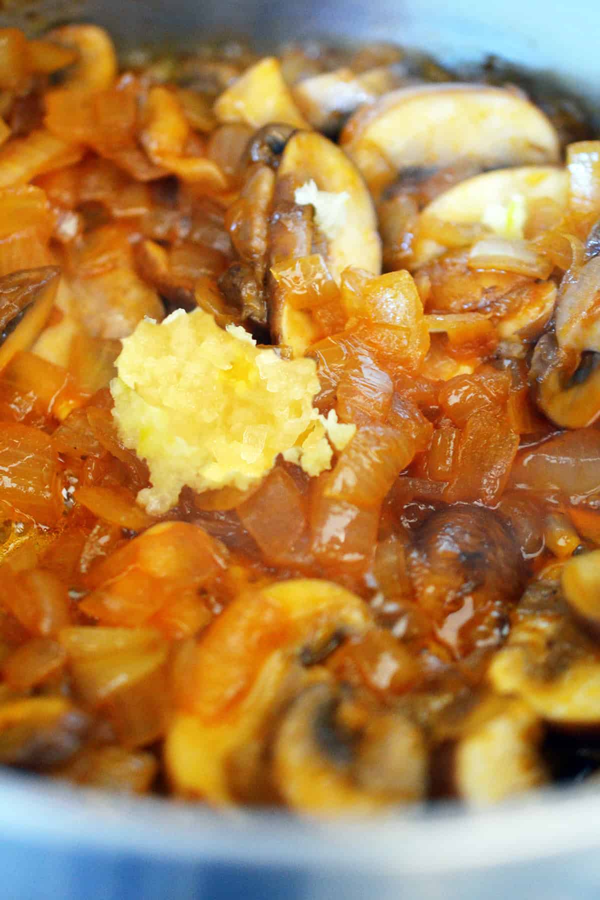 A closeup of minced garlic added to sautéed mushrooms, onions, and the other ingredients for gluten-free gravy.
