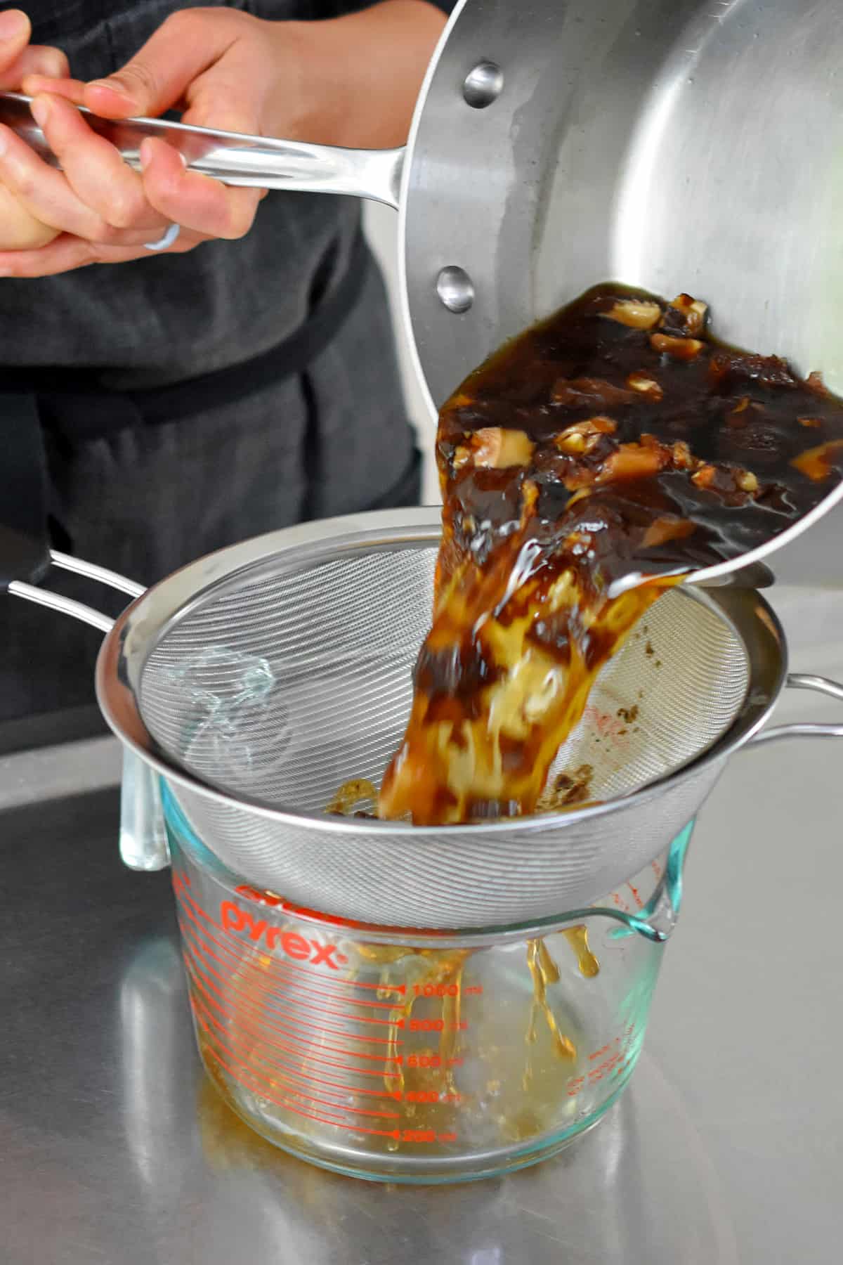 Straining vegan fish sauce through a fine mesh sieve to collect the shiitake mushrooms and dulse.
