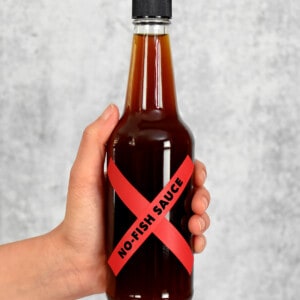 A hand is holding a bottle of homemade vegan fish sauce with a red label that says, "No-Fish Sauce"