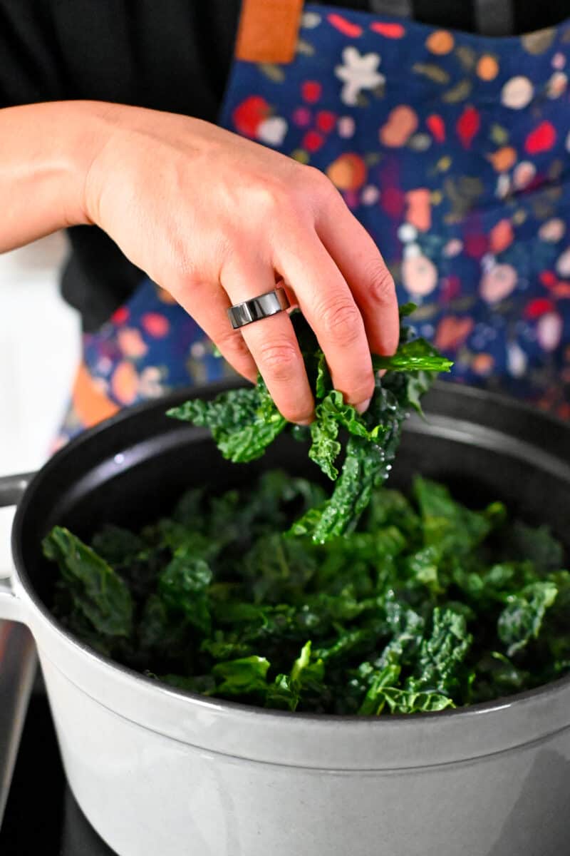 Adding chopped Tuscan kale to a simmering pot of soup.