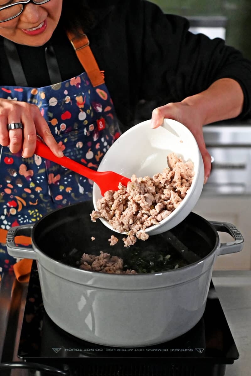 Adding cooked bulk Italian sausage into a pot of Zuppa Toscana.