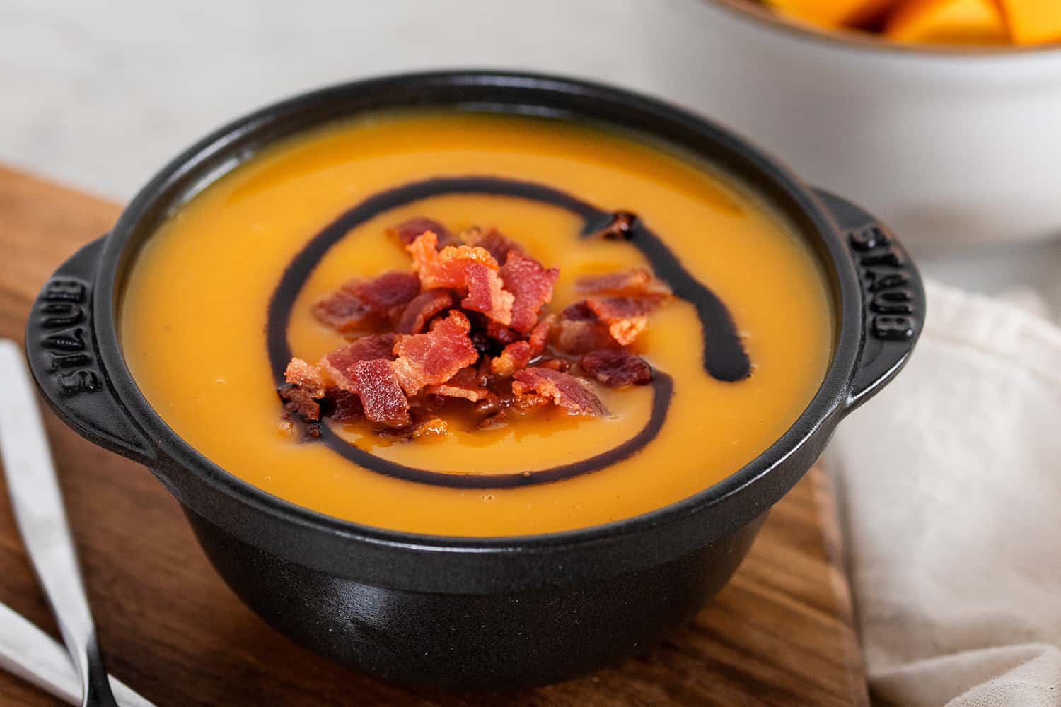 A closeup of a black bowl filled with Instant Pot Butternut Squash Soup, topped with crispy bacon bits and aged balsamic vinegar.