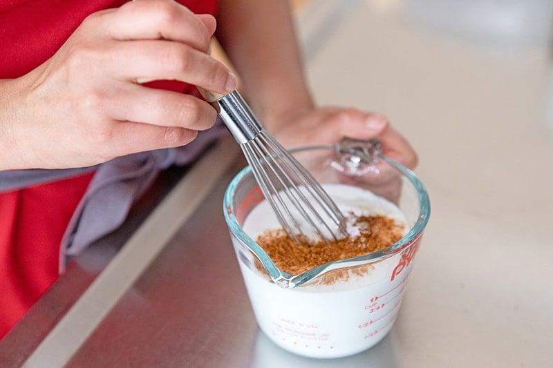 Whisking together coconut milk and tandoori spices in a measuring cup to make keto Sheet Pan Tandoori Chicken