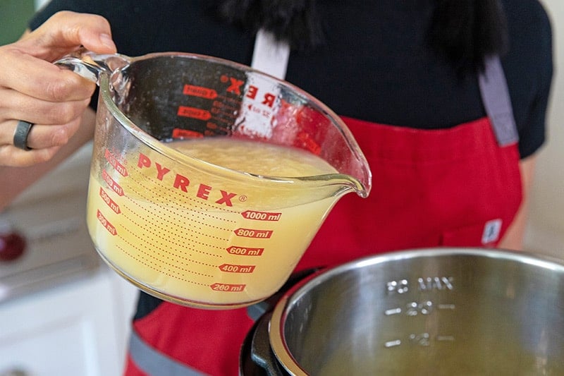 Pouring bone broth into an Instant Pot to make Instant Pot Vegetable Soup.