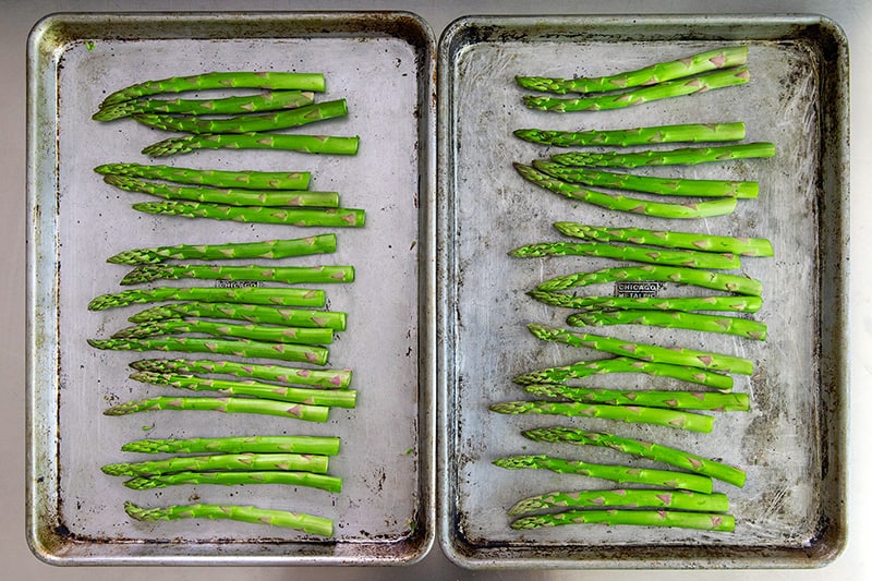 An overhead shot of the trimmed asparagus divided evenly onto two rimmed baking sheets.