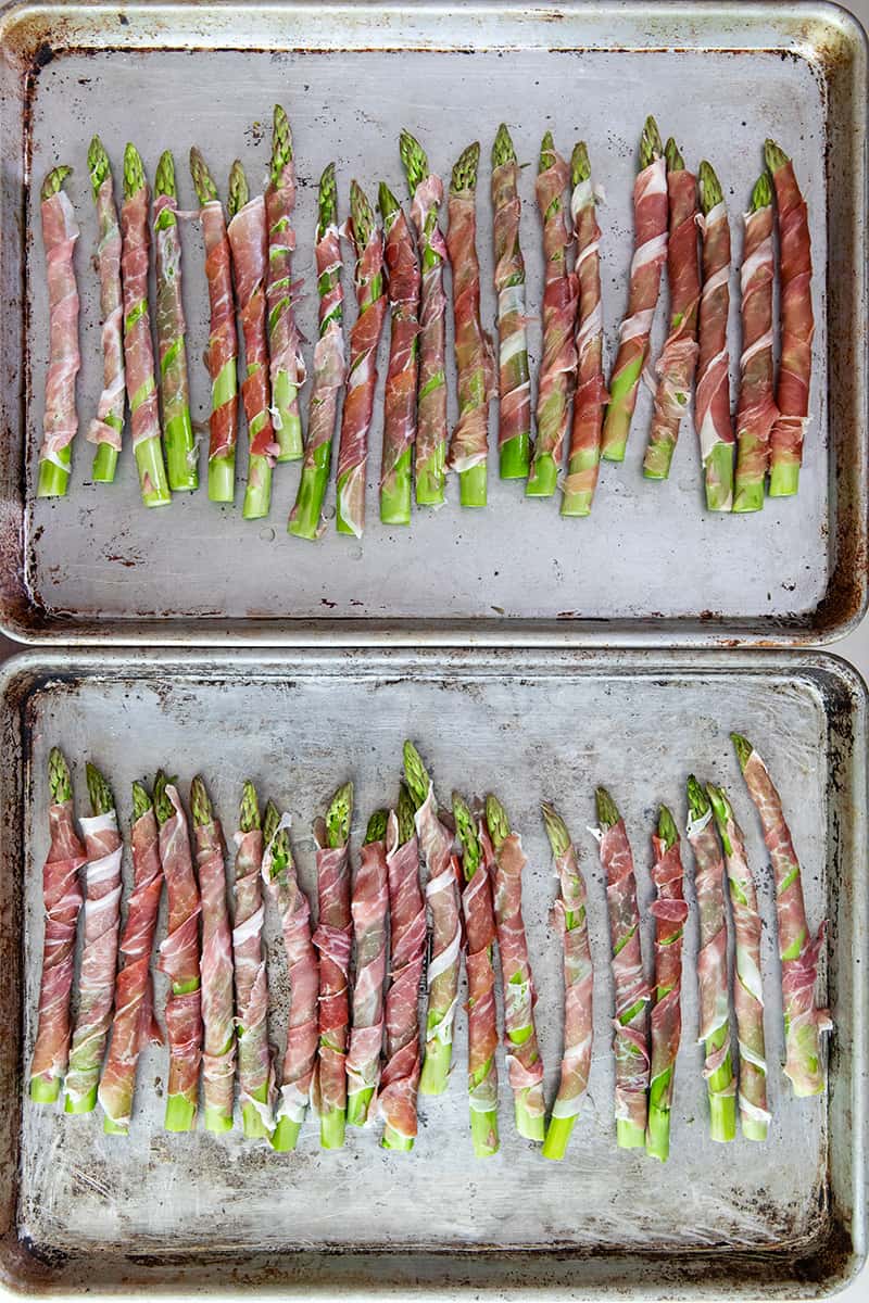 An overhead shot of two rimmed baking sheets filled with prosciutto-wrapped asparagus in a single layer.