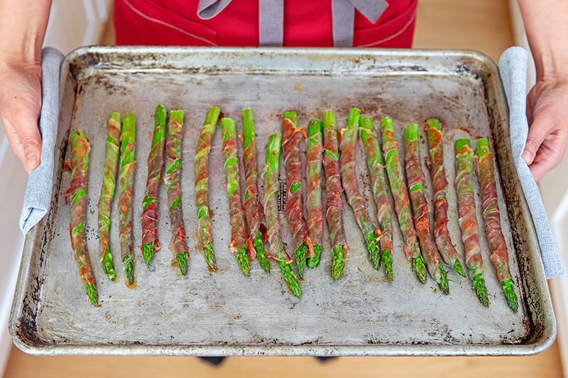 An overhead shot of a person holding a tray of prosciutto-wrapped asparagus.