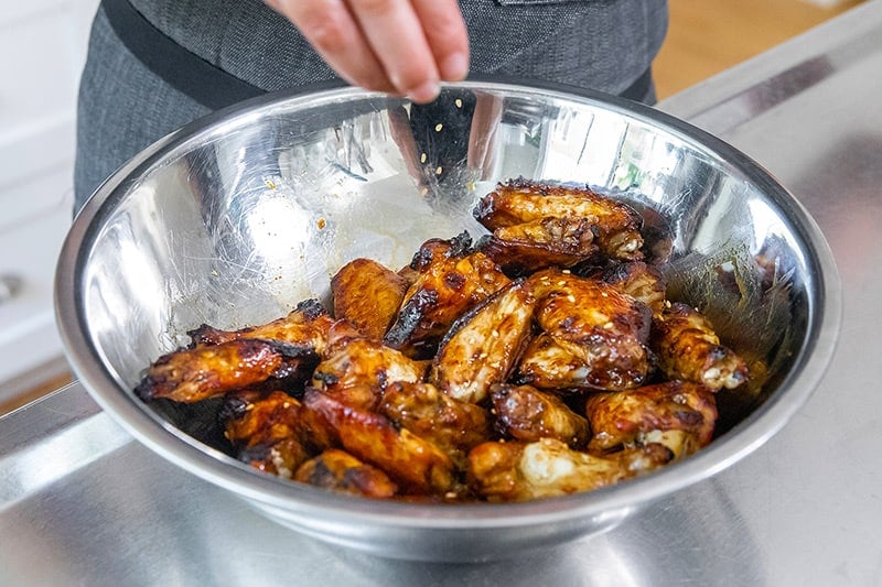 Sprinkling toasted sesame seeds on Whole30 Chinese Chicken Wings