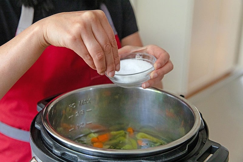 Someone adds salt to the Instant Pot Vegetable Soup.