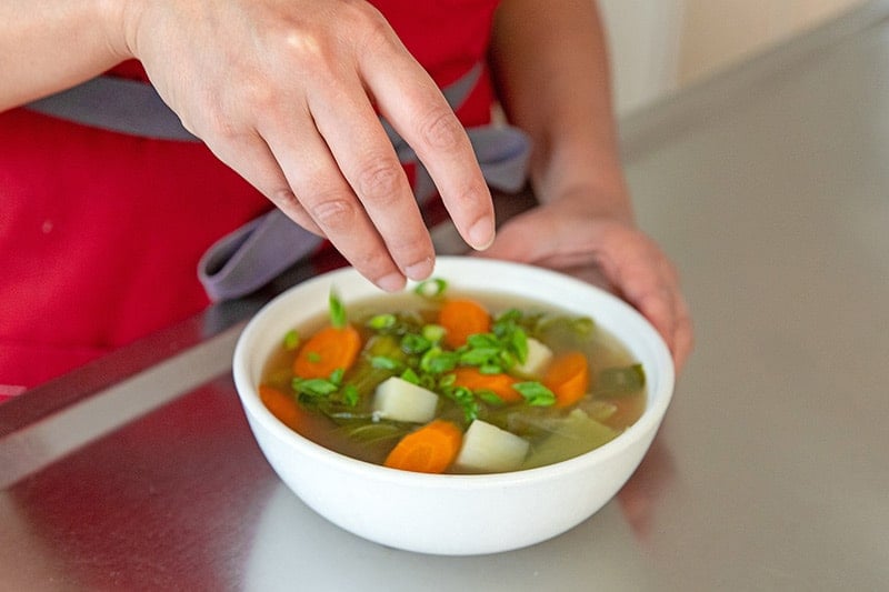 Sprinkling sliced scallions on top of Instant Pot Vegetable Soup.