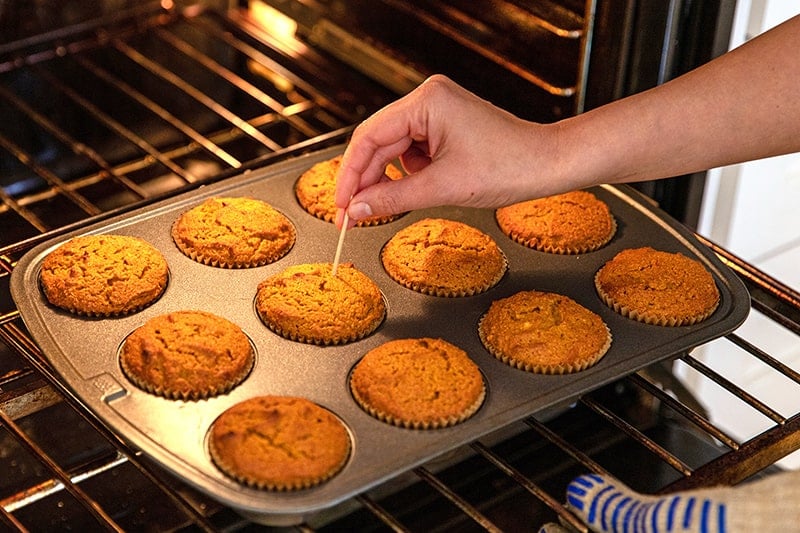 Checking the doneness of paleo pumpkin muffins by inserting a toothpick into the center of one.