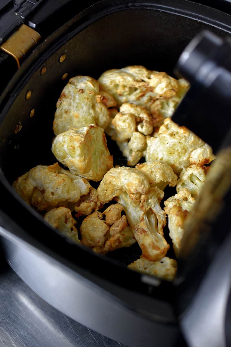 An overhead view of Buffalo Cauliflower in an air fryer basket. The florets are golden brown and ready to be sauced.