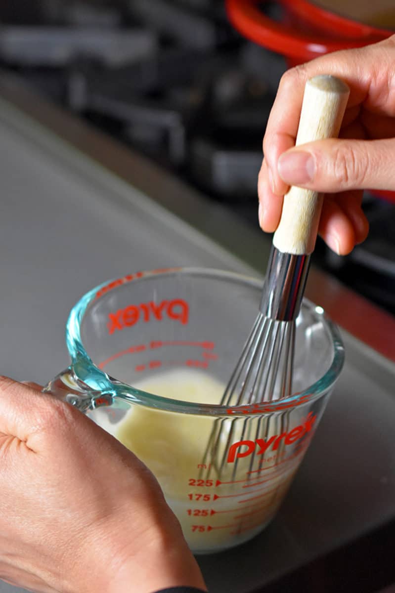 Whisking arrowroot powder with the reserved broth in a small measuring cup
