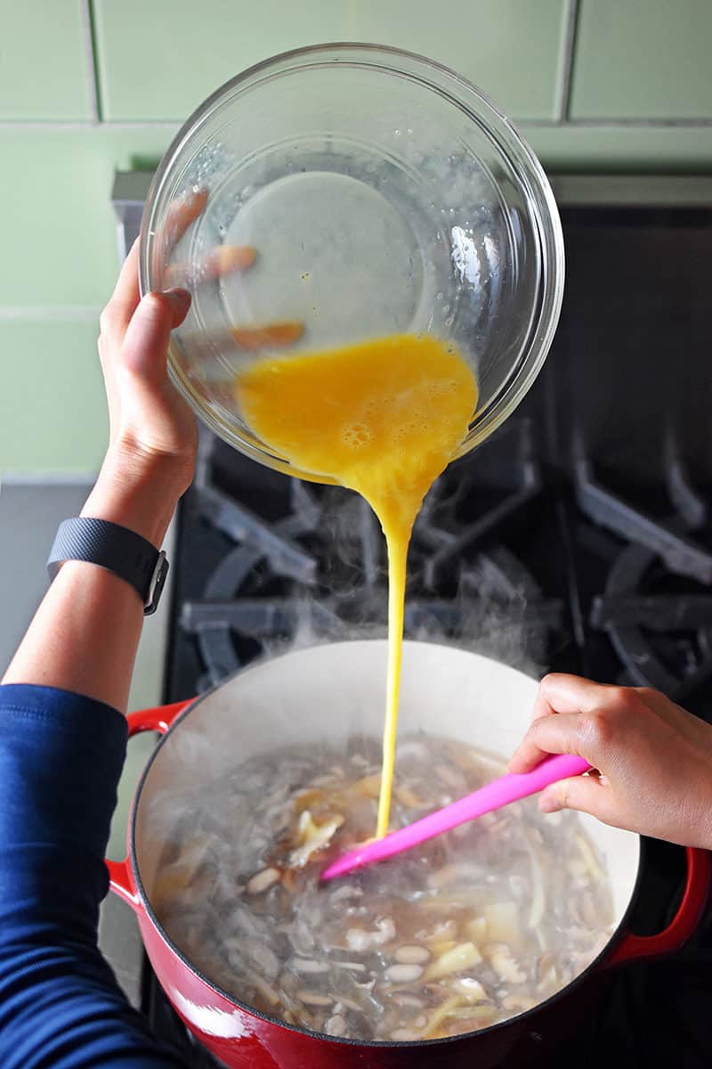 Pouring whisked eggs into the steaming pot of Hot and Sour Soup