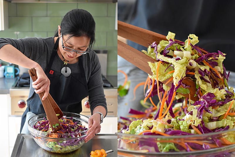 A woman is tossing Whole30-friendly Chinese Chicken Salad in a large clear bowl with wooden tongs.
