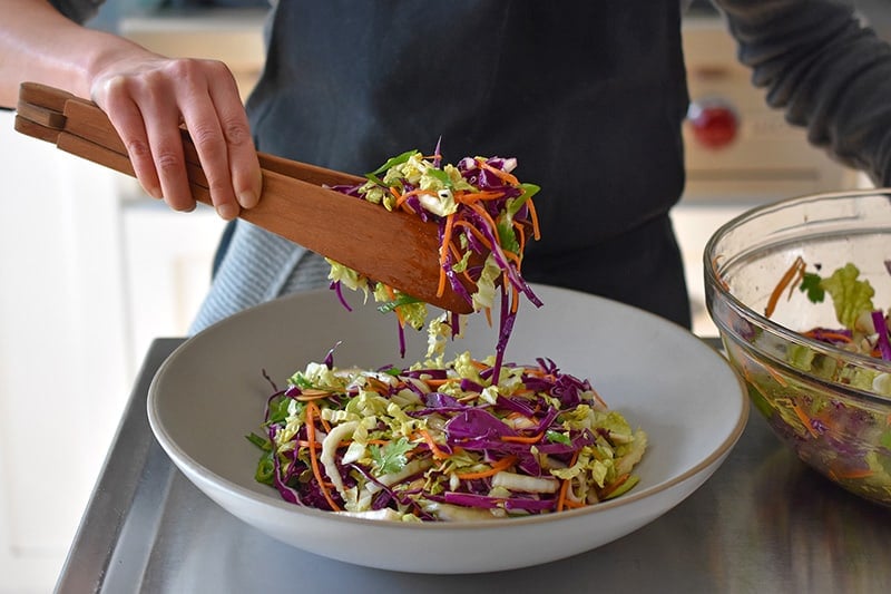 Transferring the Whole30 Chinese Chicken Salad to a large grey ceramic serving platter.