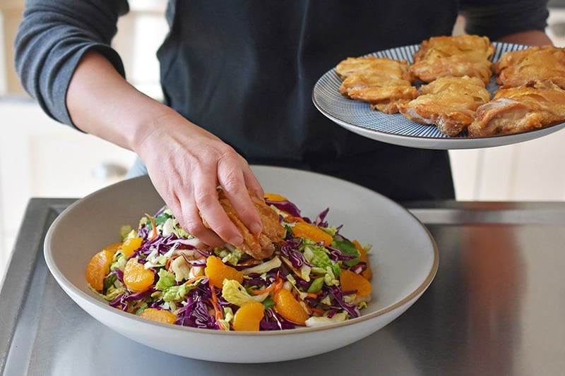 A person is placing sliced crispy chicken thighs on top of the Whole30 Chinese Chicken Salad