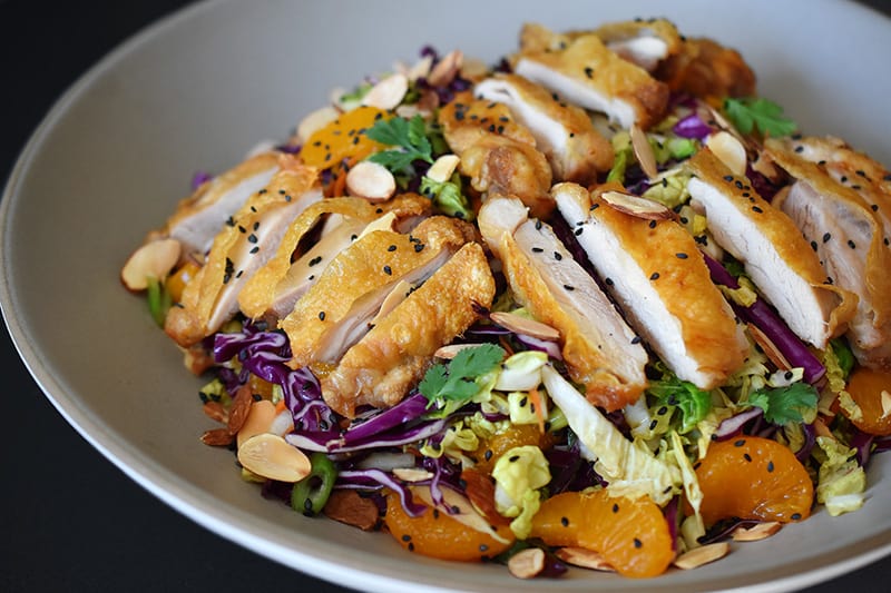 A close up of Whole30-friendly Chinese Chicken Salad, a colorful blend of cabbage, carrots, mandarin oranges, herbs, and crispy Cracklin' Chicken.