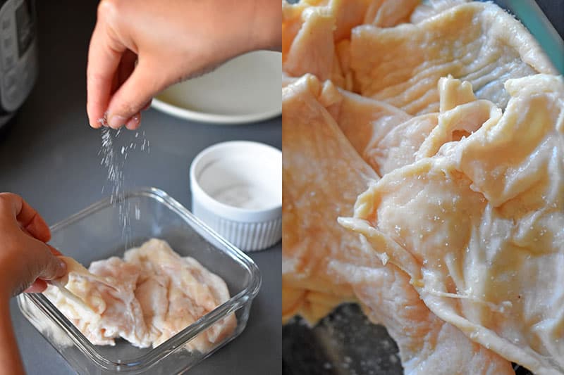 A hand is sprinkling salt on raw chicken skin.