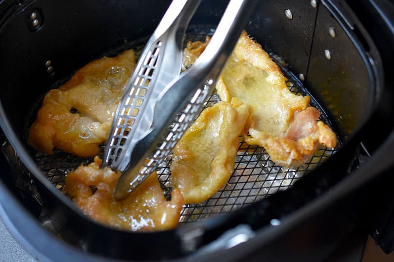 Flipping the chicken skins in an air fryer at the halfway point.