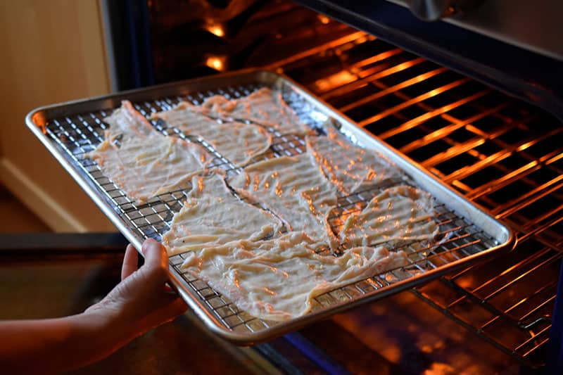 Placing a tray of chicken skins into the oven to make a keto snack.