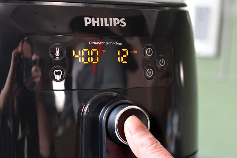 A person is programming an air fryer to cook at 400°F for 12 minutes 