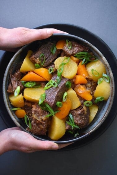 An overhead shot of a two hands holding a bowl of Instant Pot Chinese Beef Stew.