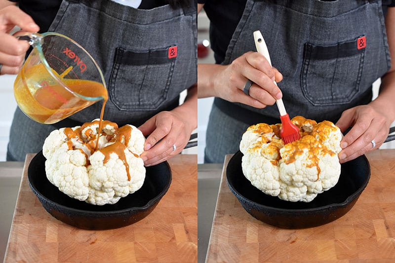 Someone pouring and brushing Whole30 Nom Nom Paleo Tandoori marinade on a whole cauliflower head.