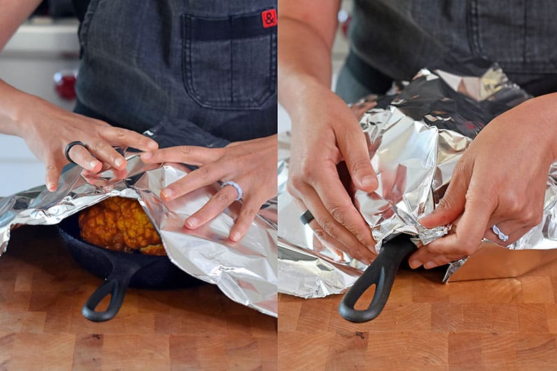 Someone covering Tandoori Whole Roasted Cauliflower with aluminum foil.