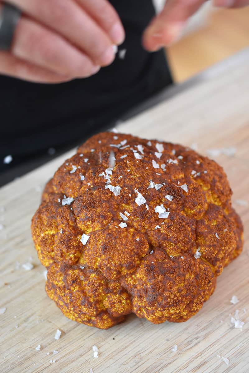 An overhead shot of someone sprinkling salt on top of Tandoori Whole Roasted Cauliflower