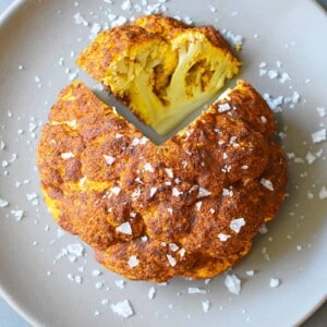An overhead shot of Tandoori Whole Roasted Cauliflower on a brown plate with a wedge sliced out of it.