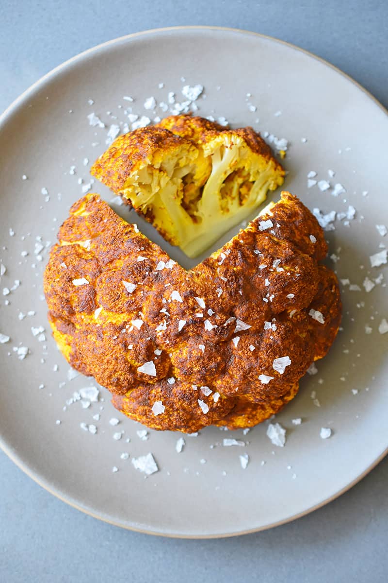 An overhead shot of Tandoori Whole Roasted Cauliflower on a brown plate with a wedge sliced out of it.