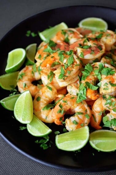 A side shot of Tandoori Shrimp on a black platter with lime wedges on the side.