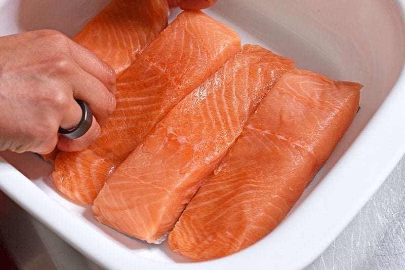 Four salmon fillets are placed in a snug fitting white dish with high sides.
