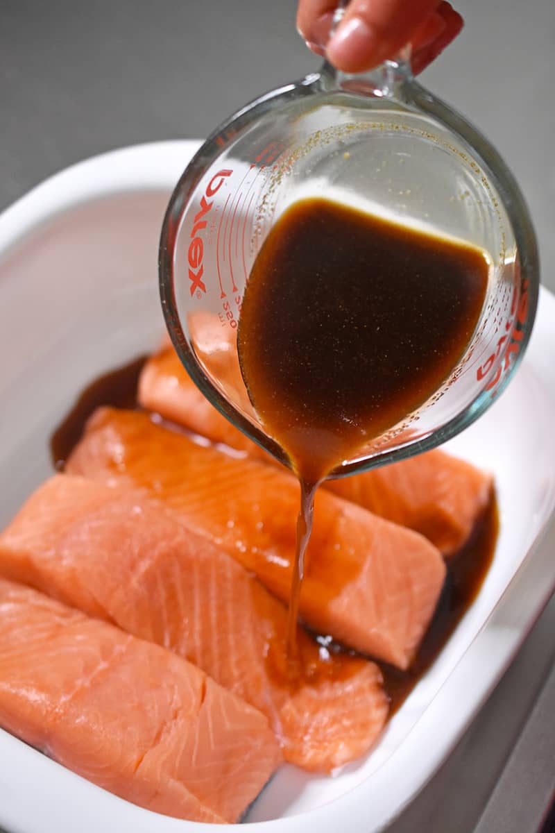 Pouring All-Purpose Stir-Fry Sauce over the salmon fillets to make Easy Teriyaki Salmon, a healthy Whole30 dinner.