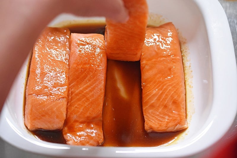Someone is flipping the salmon fillets in the All-Purpose Stir-Fry Sauce to coat them.