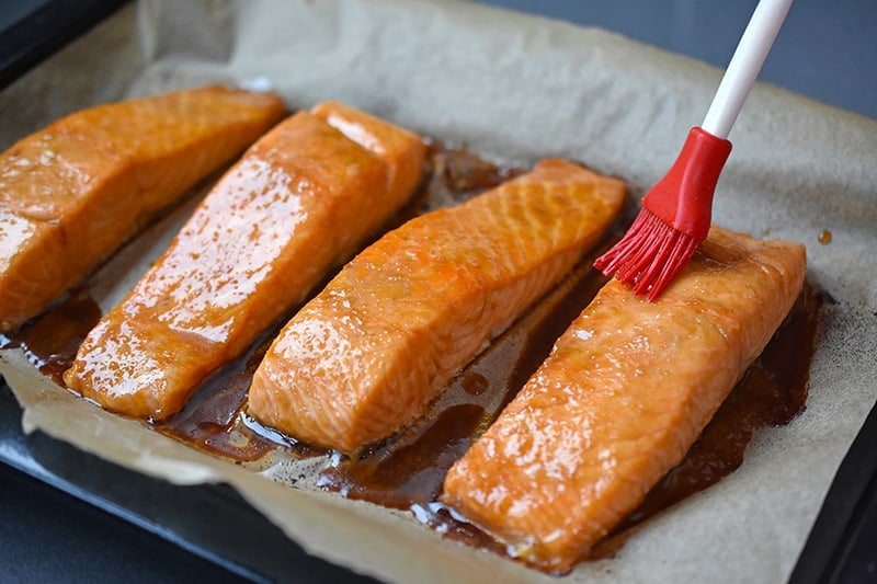 A brush is adding reserved All-Purpose Stir-Fry Sauce on the easy teriyaki salmon, a healthy Whole30 friendly dinner.