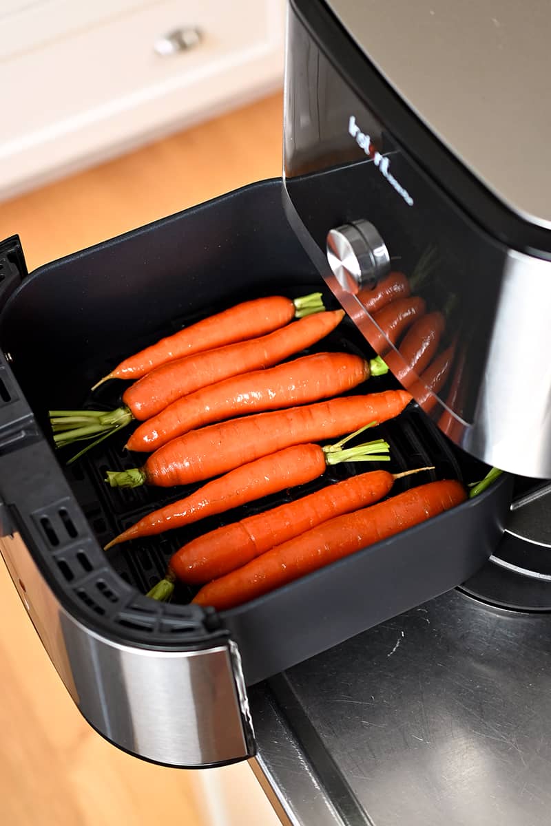 Seasoned raw carrots are in an open air fryer basket.