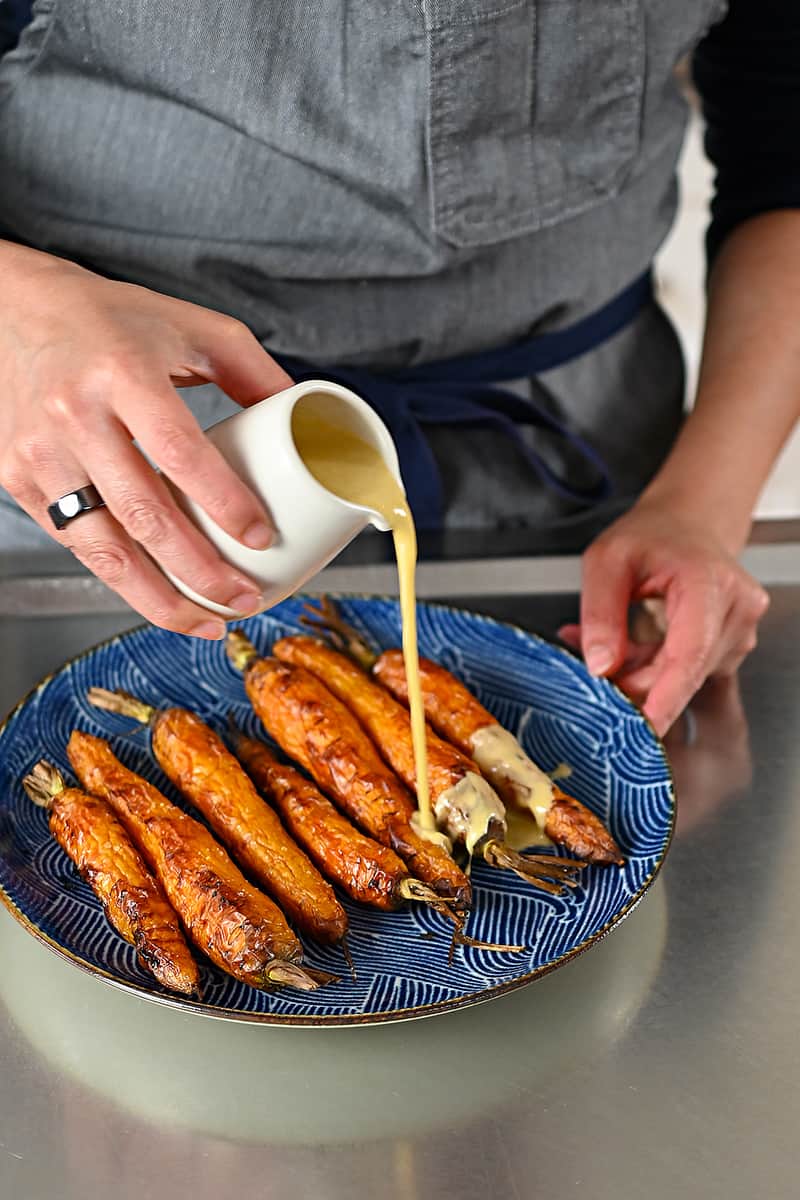 Pouring sesame ginger dressing on a plate of air fryer roasted carrots.