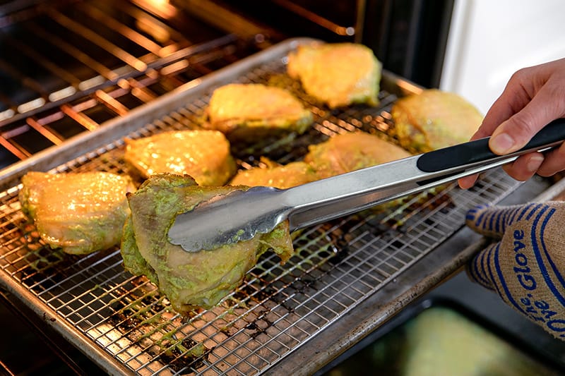 Someone flipping the chicken thighs skin-side up at the halfway roasting point.