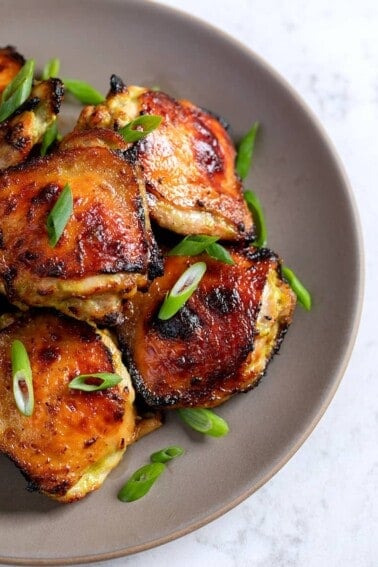 An overhead shot of a platter of Asian Chicken Thighs topped with sliced scallions.