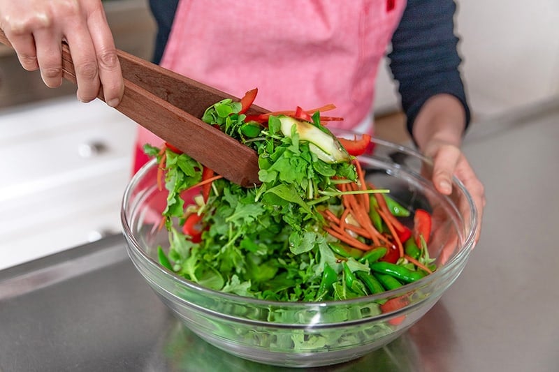 Tossing the Asian steak salad and the dressing with wooden tongs.