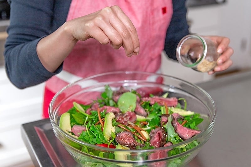 Sprinkling toasted sesame seeds on top of paleo and Whole30 Asian Steak Salad.
