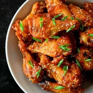 An overhead shot of a bowl filled with Asian Sticky Wings topped with sesame seeds and sliced scallions.