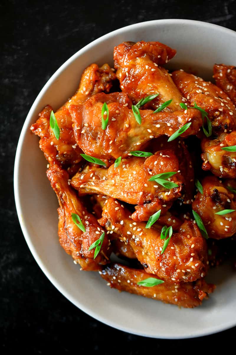 An overhead shot of a bowl filled with Asian Sticky Wings topped with sesame seeds and sliced scallions.