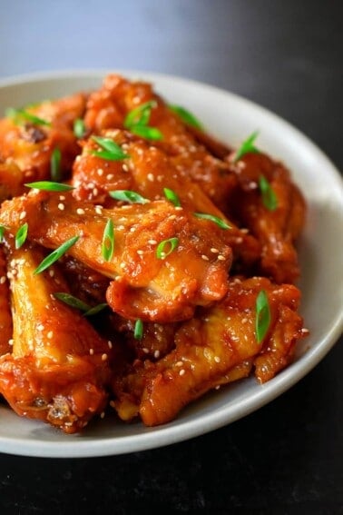 A closeup side view bowl of Asian Sticky Wings topped with sliced scallions and toasted sesame seeds.