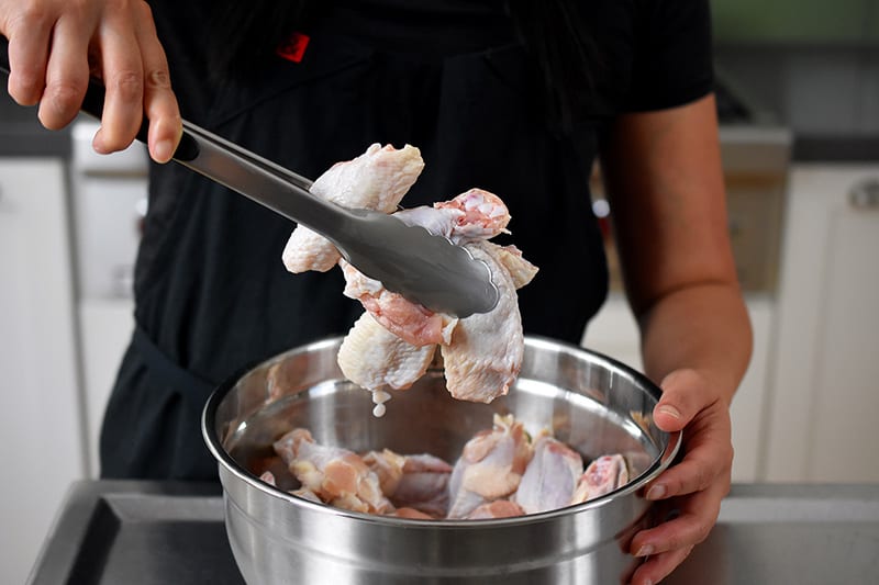 Tossing chicken wings in grain-free paleo baking powder with a pair of tongs.