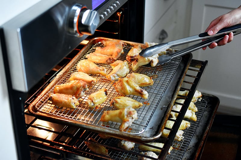 Someone using tongs to flip the chicken wings before rotating the trays in the oven.